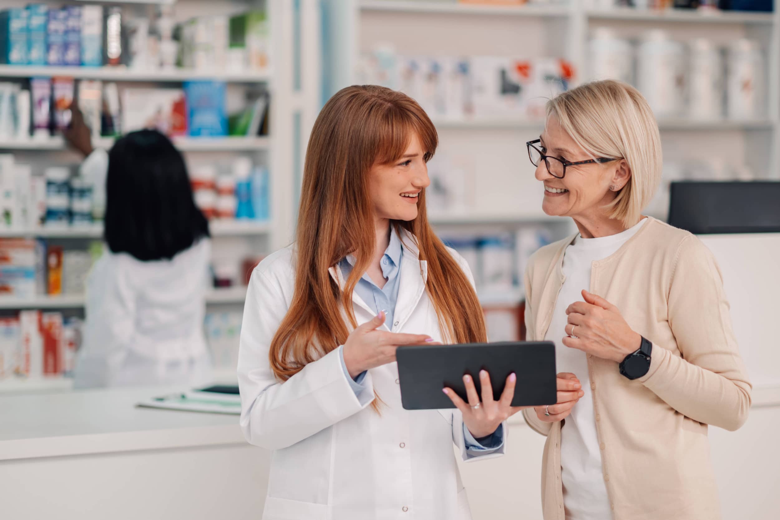 Apothekerin nutzt digitales Tablet und hilft älteren Kunden in der Apotheke